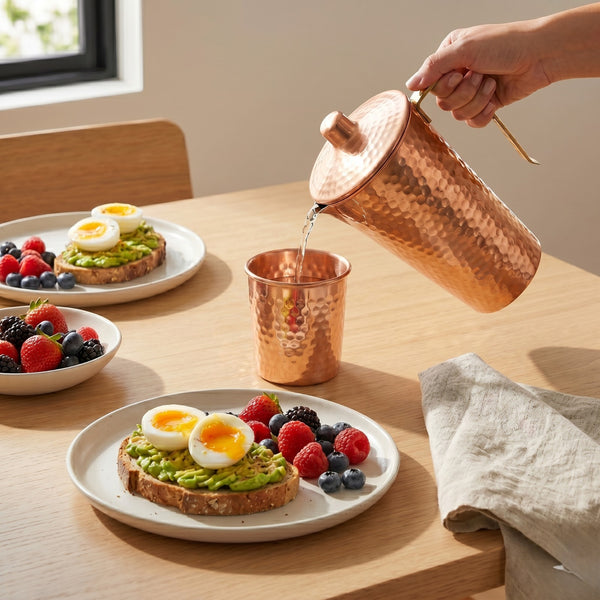 Water poured from a hammered copper pitcher into a copper cup on a breakfast table.