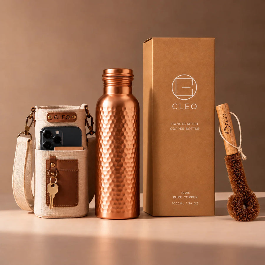 A Cleo hammered copper bottle beside its kraft gift box, canvas travel sleeve and coir cleaning brush.